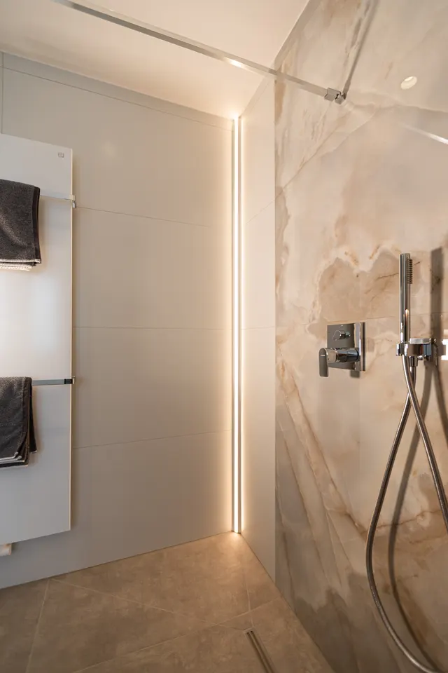 Walk-in-Dusche mit Lichtleiste, Marmoroptik und Handtuchheizkörper nach einer Badsanierung in Wadersloh